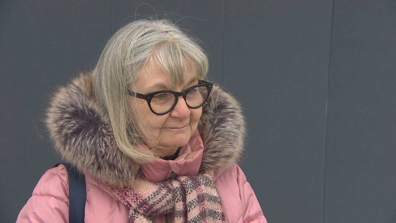 A woman in a pink coat, with a furry hood, looks forward.