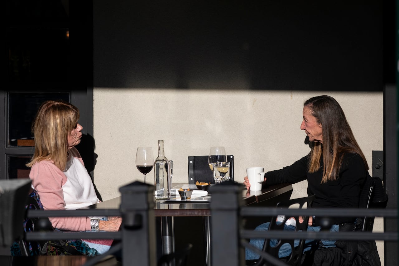 Two older women diners seated at an outdoor restaurant patio enjoy wine and a warm beverage on a sunny afternoon in Vancouver. 
