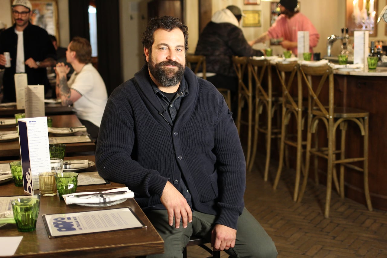 A man wearing a blue cardigan sits at a table in an Italian restaurant.