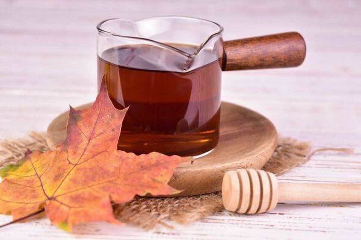 Maple syrup in a glass container against the background of maple leaves. Close-up.