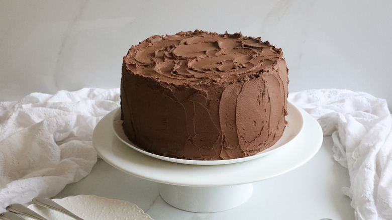 Devil's food cake on a white cake stand surrounded by white tablecloth