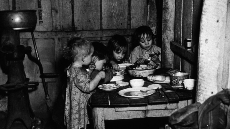 Children eating Christmas dinner around a small wooden table in a tenant farmer's house in Southeastern Iowa