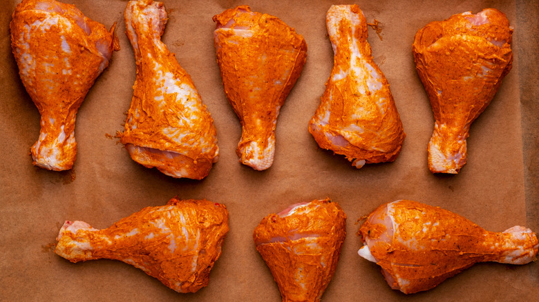 Raw chicken drumsticks in marinade on a baking sheet in the oven