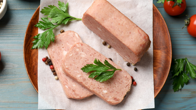 canned meat on baking paper on round wooden tray next to tomatoes and parsley leaves