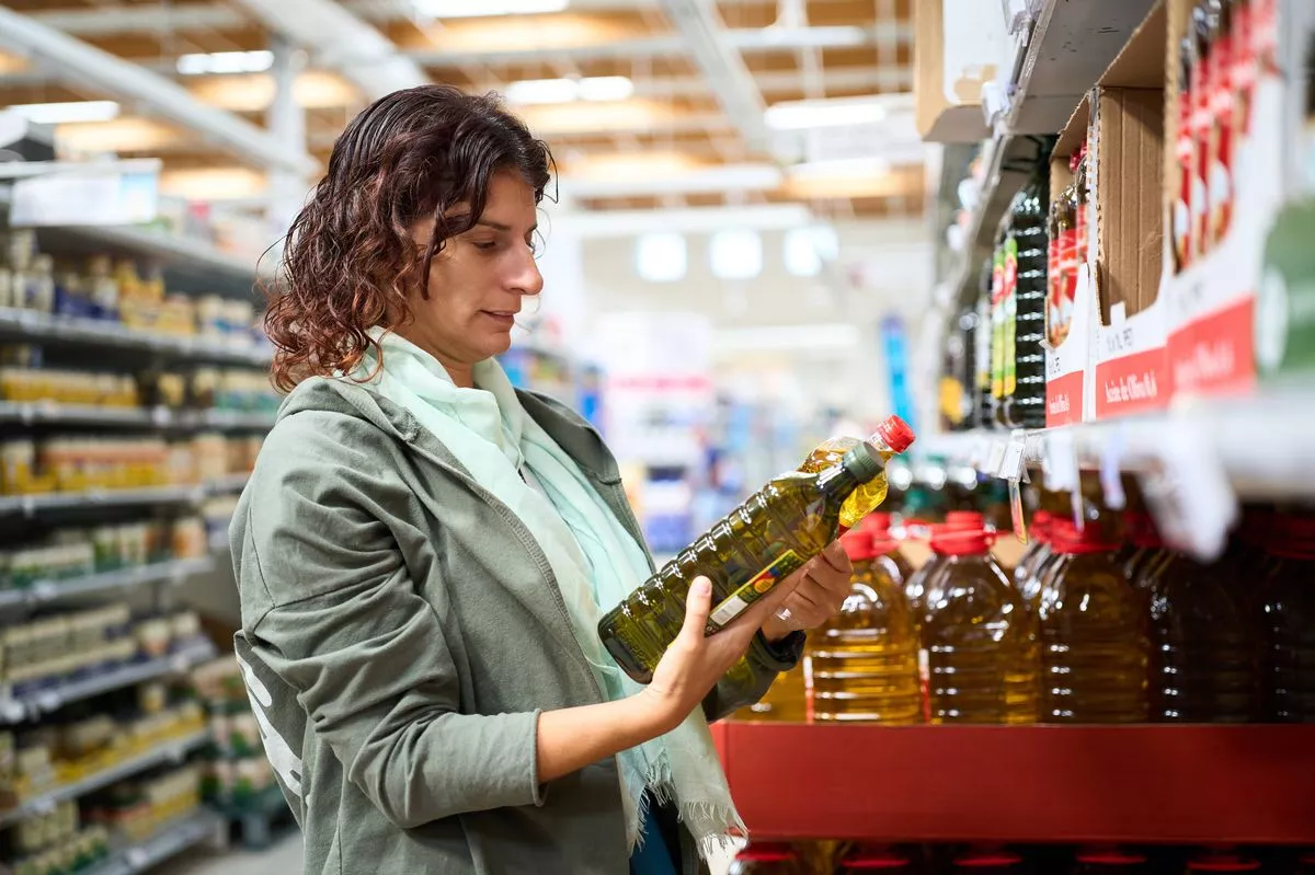 Woman in a grocery comparing prices of different olive oil bottles