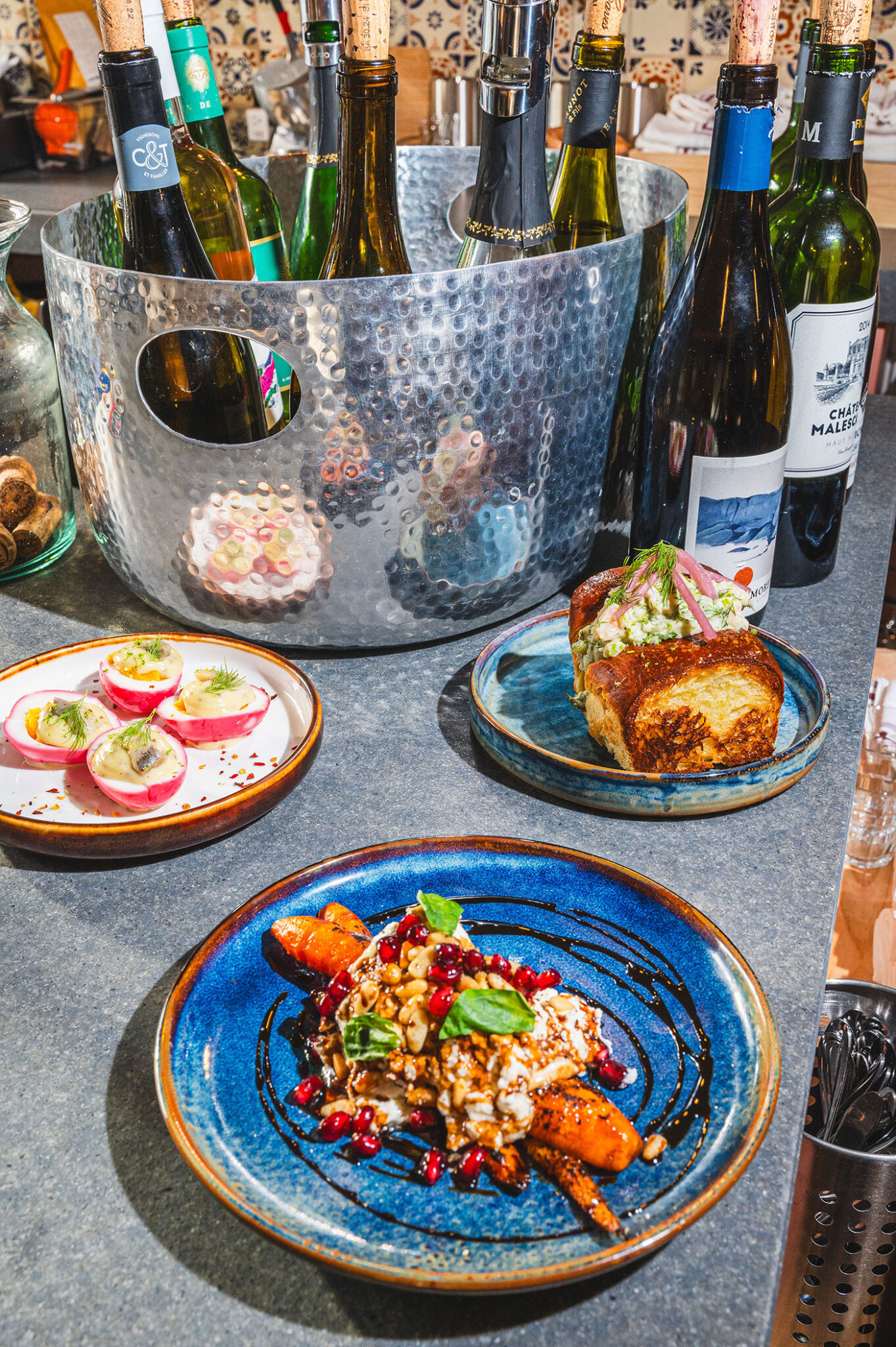 Dishes sit on a countertop in front of bottles of wine.