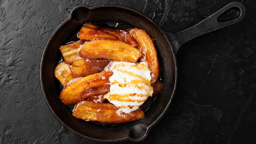 Homemade fried bananas foster with cinnamon and ice cream in cast iron pan