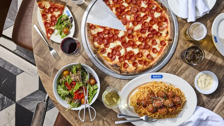 Overhead view of several dishes, including a pepperoni pizza, spaghetti and meatballs, and a salad, served at Naples Ristorante E Bar, a popular Italian restaurant located inside Downtown Disney, a district within Disneyland Resort in Anaheim, California.