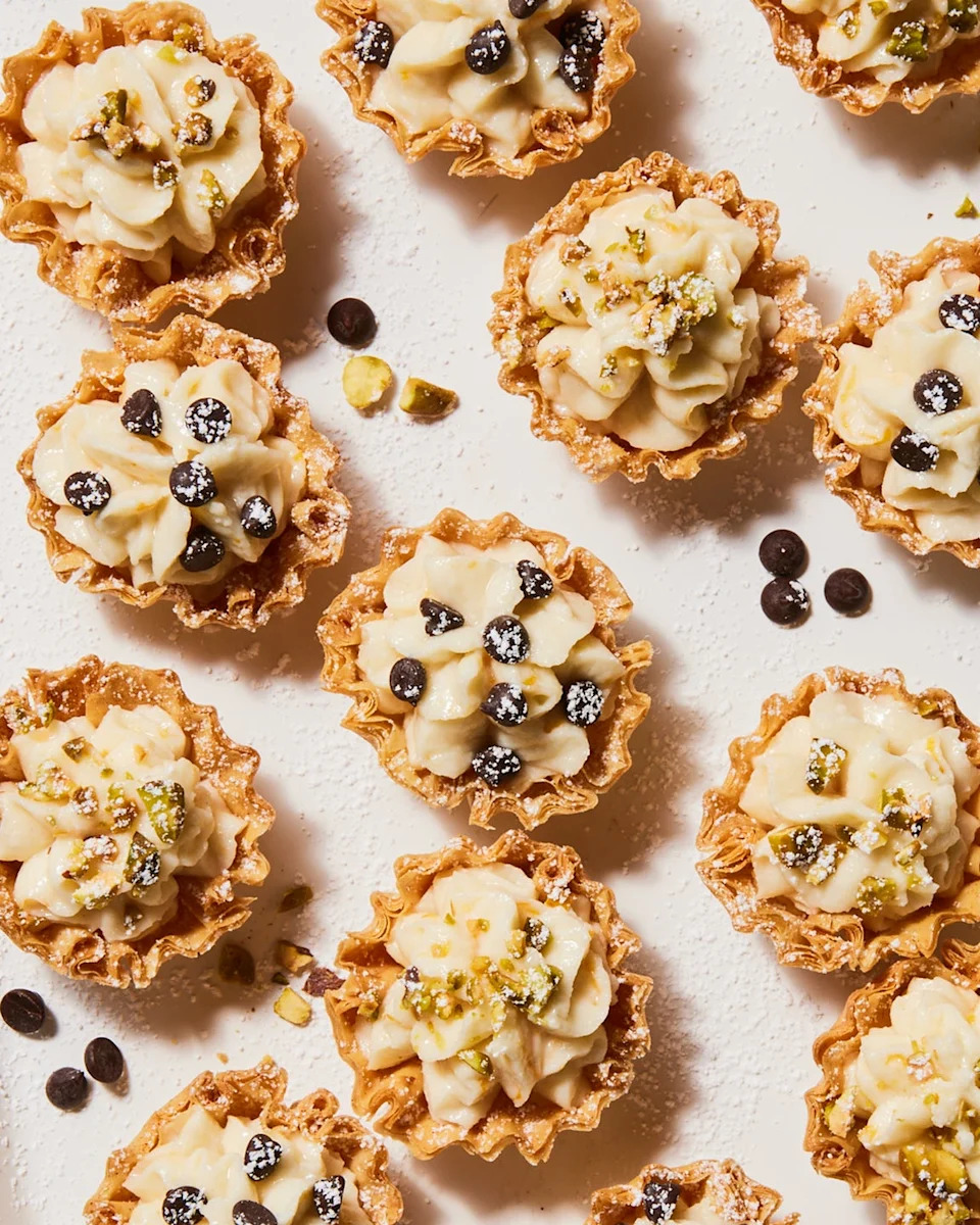 individual cannoli bites topped with chocolate chips, crushed pistachio and powdered sugar