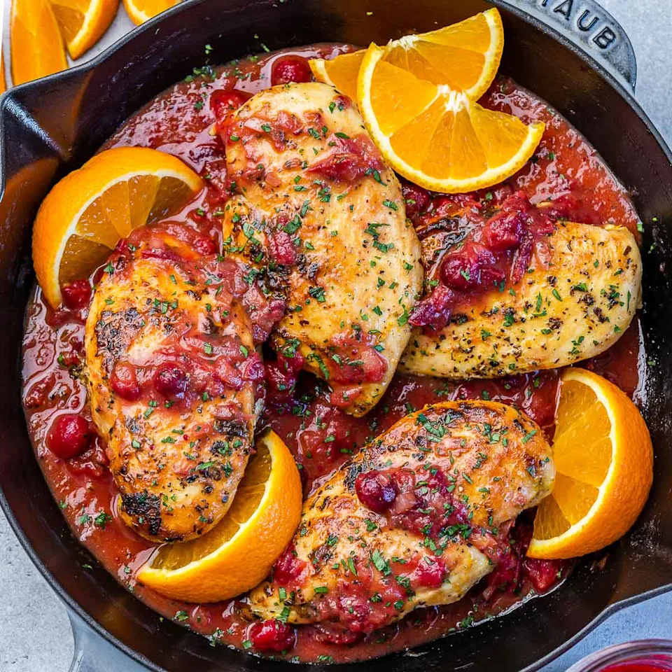 chicken breasts in cranberry sauce in skillet with orange wedges. 