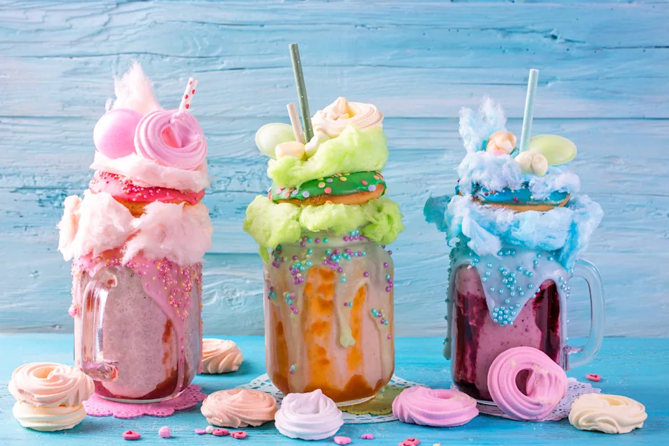 Three mason jars filled with extravagant milkshakes, topped with cotton candy, donuts, and colorful sweets