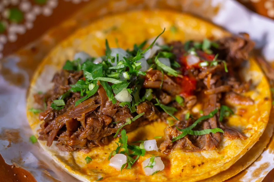 Taco with shredded meat, topped with chopped onions and cilantro, served on a soft tortilla