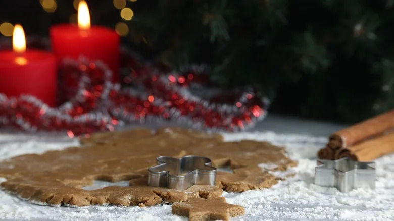 Gingerbread cookie dough sitting next to cinnamon sticks and burning festive candles
