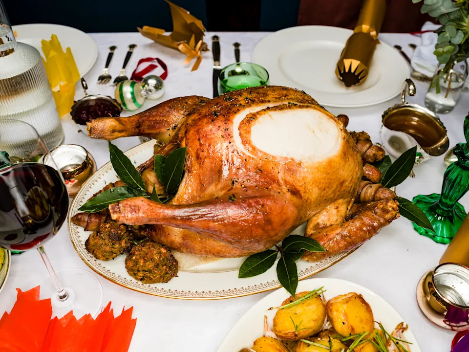 Close Up Traditional Roasted Turkey On Christmas Dinner Table With Red Wine, Potatoes And Christmas Crackers