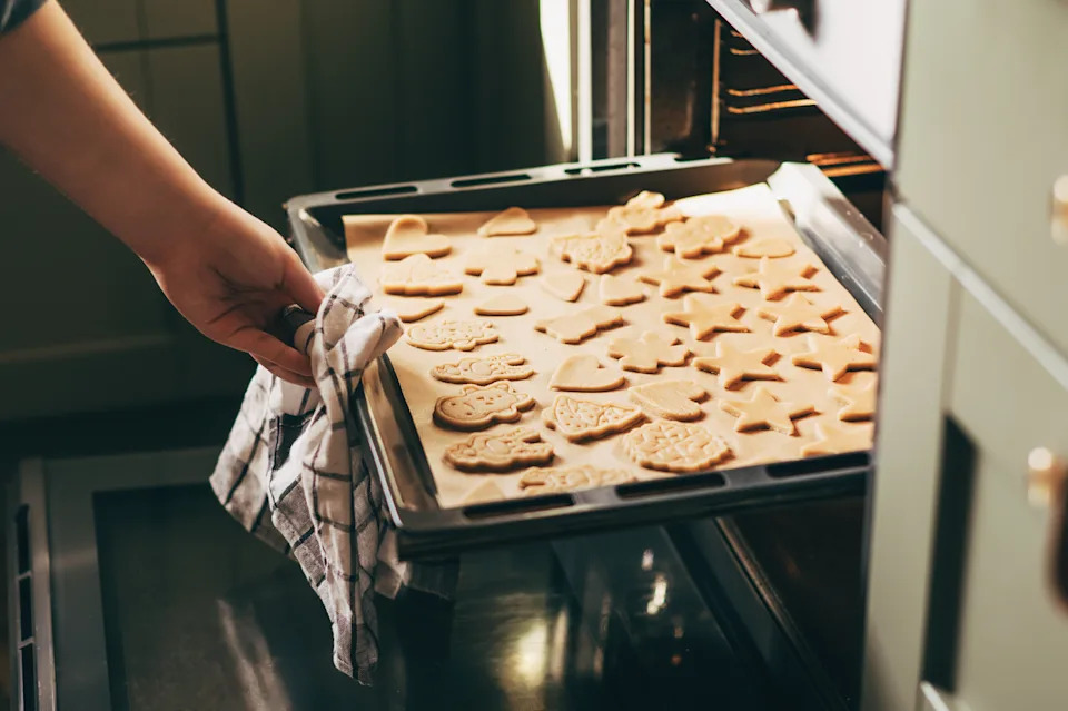 Woman putting tray with christmas cookies in oven close up in modern kitchen. Baking gingerbread cookies. Family holiday preparation, xmas culinary. Biscuits recipe