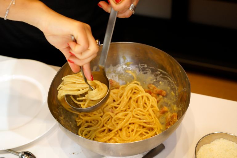 A woman spoons onto a plate some "spaghetti alla Carbonara" during a cooking competition on the eve of the Carbonara Day