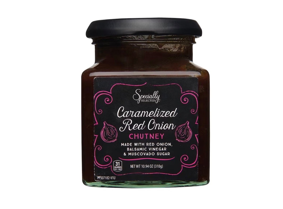 A jar of Specially Selected Caramelized Red Onion Chutney with a black lid and a black label featuring pink accents and text describing the chutney's ingredients: red onion, balsamic vinegar, and muscovado sugar.