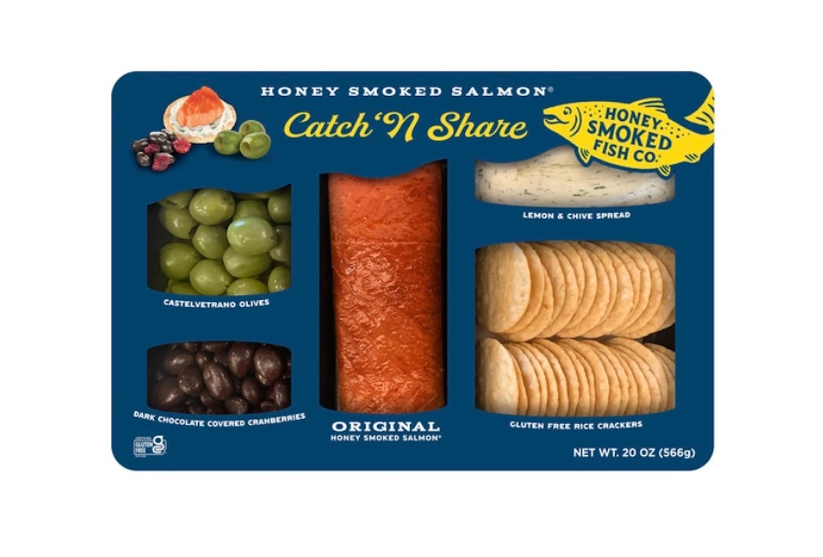 A platter with honey smoked salmon, green Castelvetrano olives, lemon and chive spread, dark chocolate covered cranberries, and gluten free rice crackers in separate sections. Packaging is labeled "Catch 'N Share".