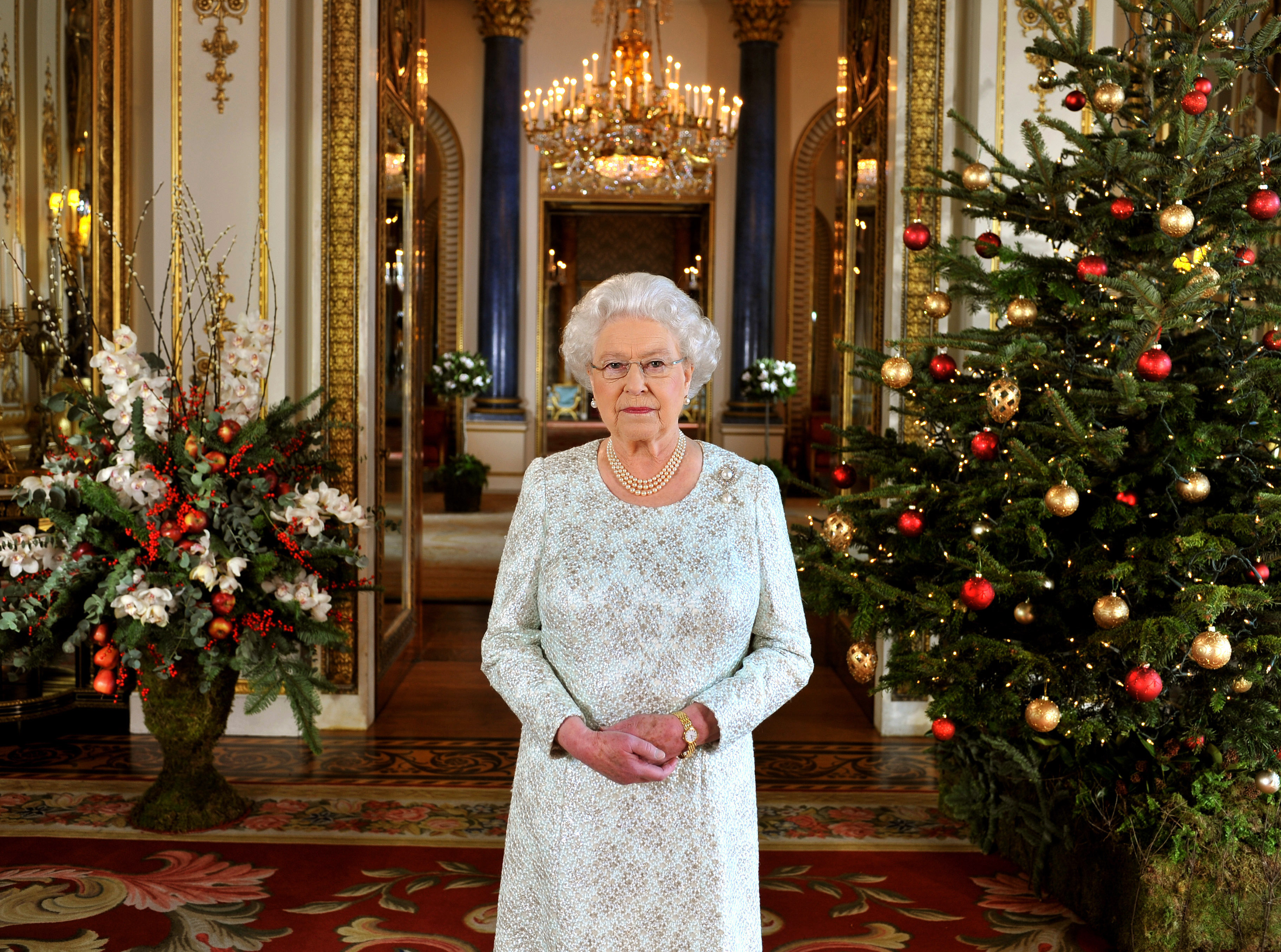 Queen Elizabeth in 2012 standing between decorated Christmas trees, wearing a white dress