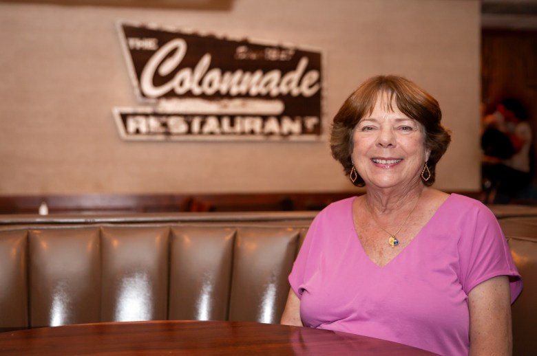 Patsy Moss, a longtime regular of The Colonnade in Atlanta, sits in a half-moon booth smiling in a pink t-shirt.