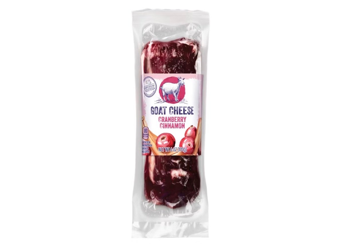 A vacuum-sealed package of goat cheese with cranberry and cinnamon flavor. The label shows a goat illustration and images of cranberries and cinnamon sticks.