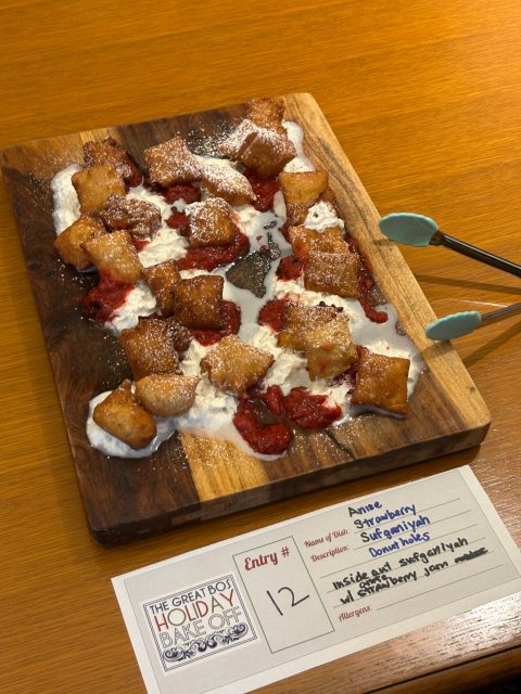A wooden board with fried dough bites, whipped cream, and strawberry jam, with metal tongs on the side. A contest entry card labeled "Strawberry Sugarpillows" is in front.