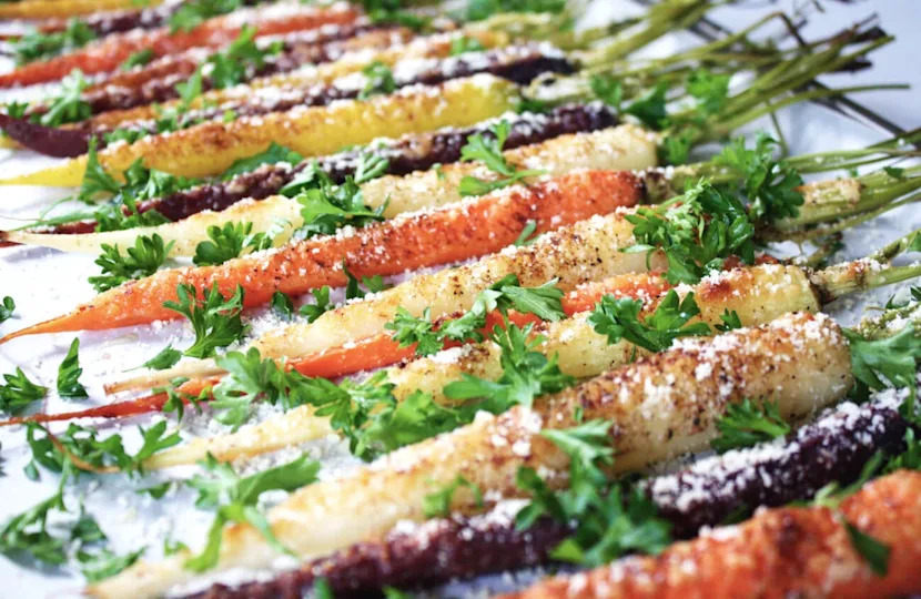 Side angle shot of rainbow carrots garnished with parsley and Parmesan cheese.