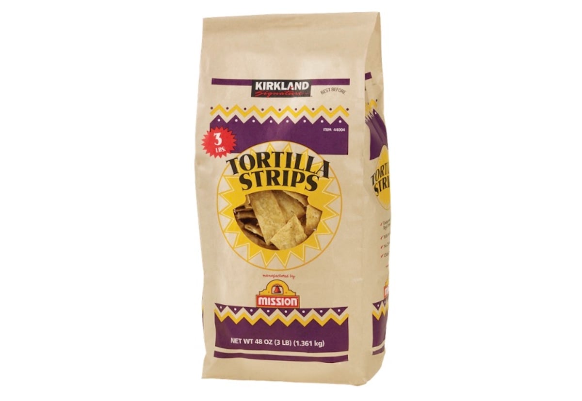 A large beige bag of Kirkland Tortilla Strips featuring Mission branding, with a clear window showing the chips inside. The bag is labeled 48 oz and decorated with red, purple, and yellow accents.