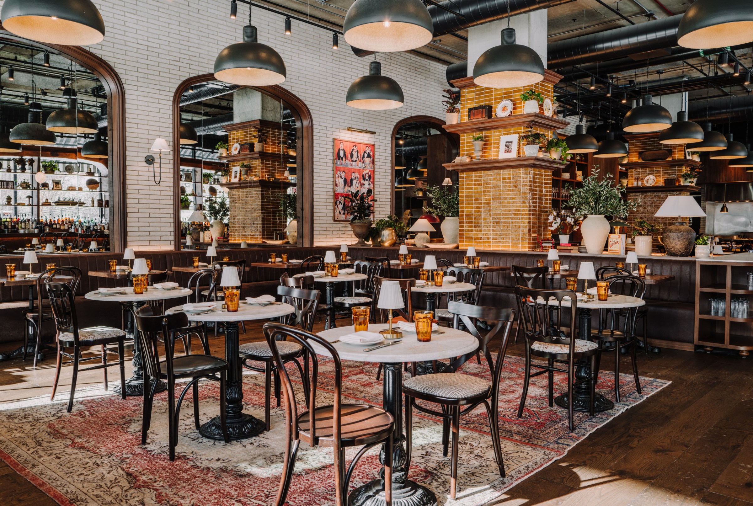 A dining area with hanging lights, two-top tables, and large mirrors on the wall.