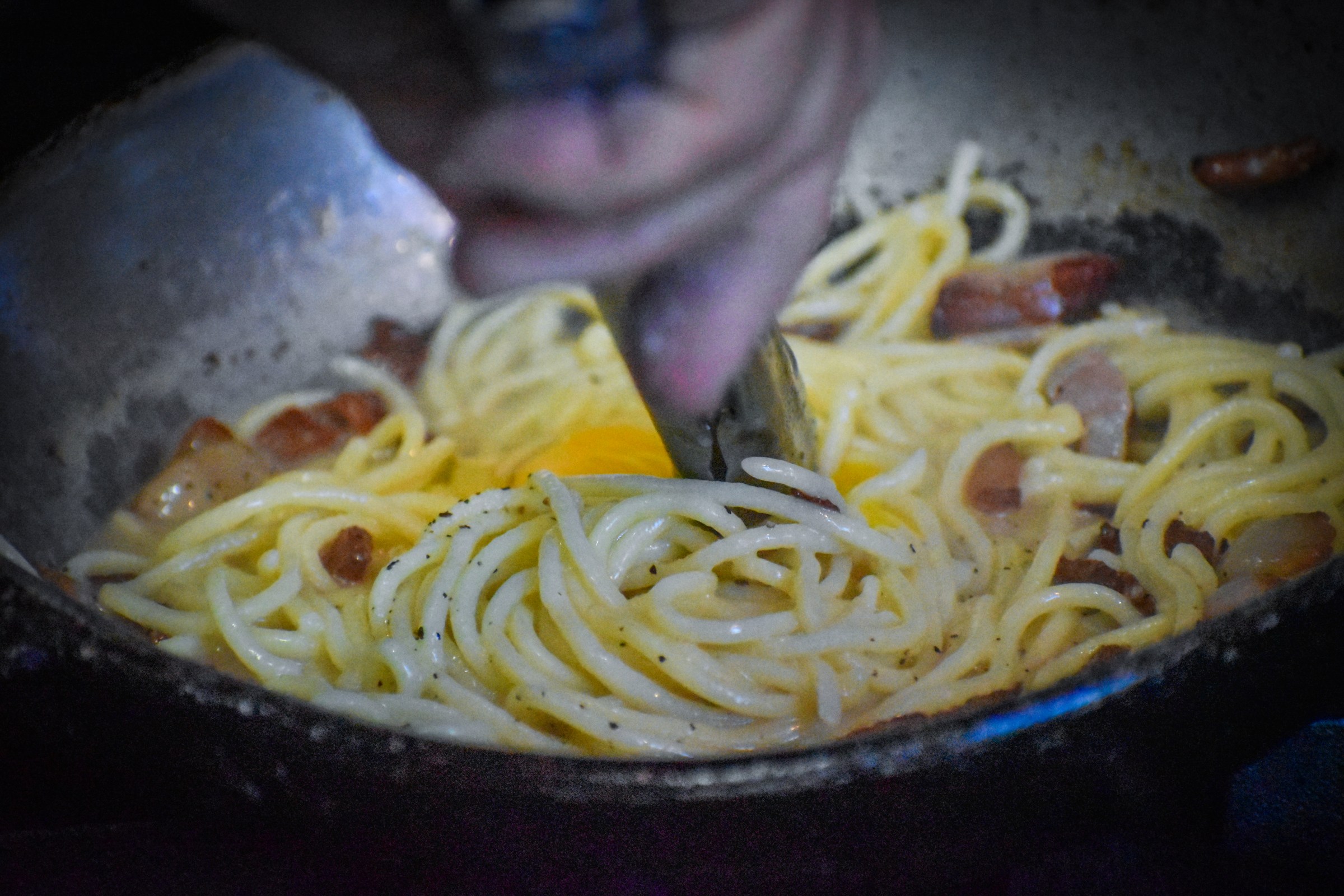 A pair of tongs tossing spaghetti with egg yolk and bacon to make carbonara at La Parolaccia.
