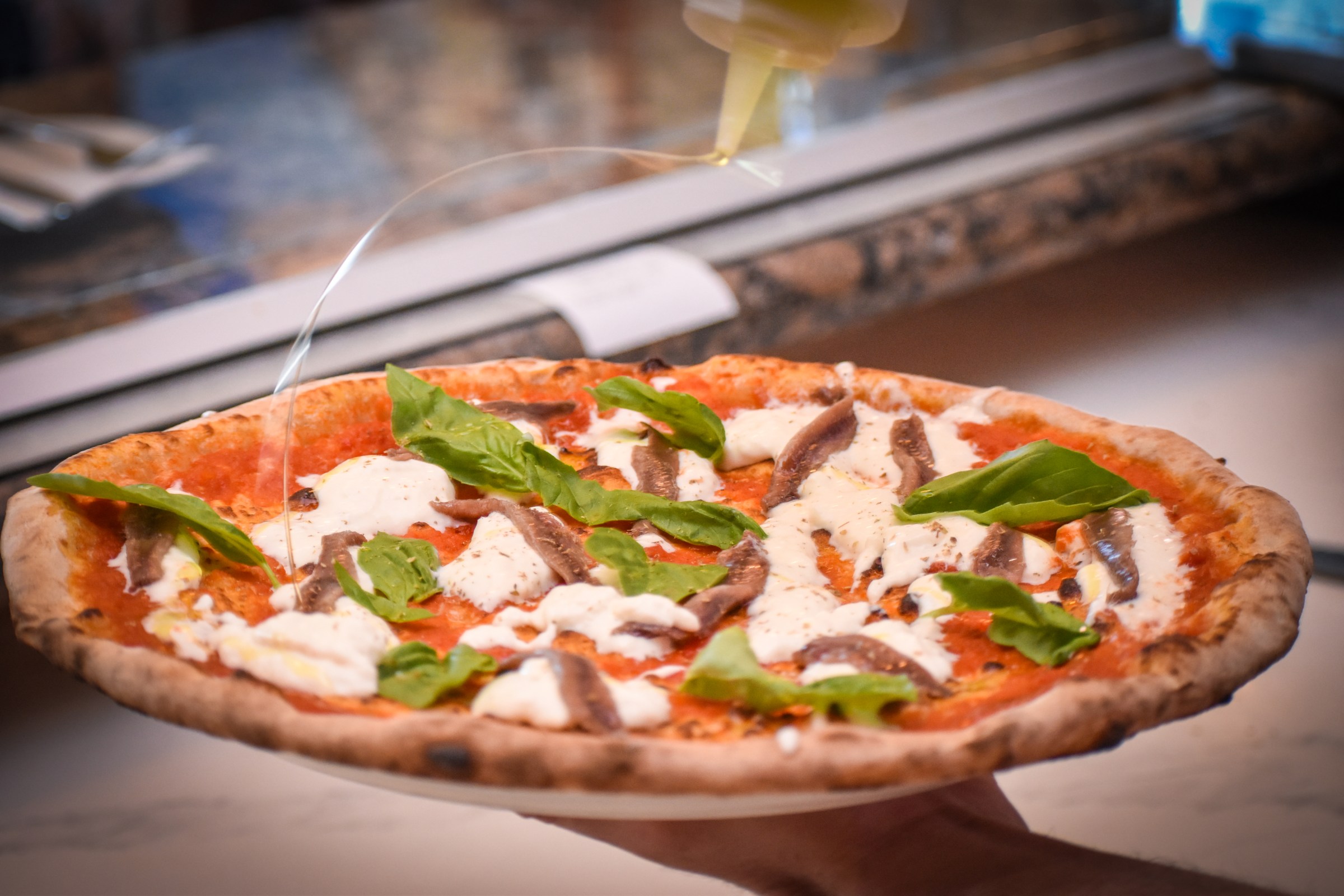 Drizzling olive oil on an anchovy-topped pizza at La Parolaccia.