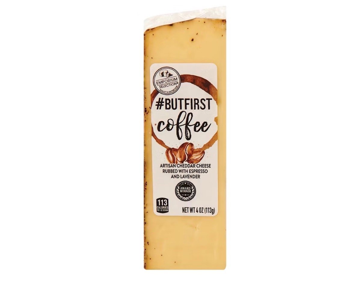 A rectangular block of cheese with a white label that reads “#BUTFIRST coffee, artisan cheddar cheese rubbed with espresso and lavender.” The cheese has dark specks on the outer edge. Net weight: 4 oz (113g).