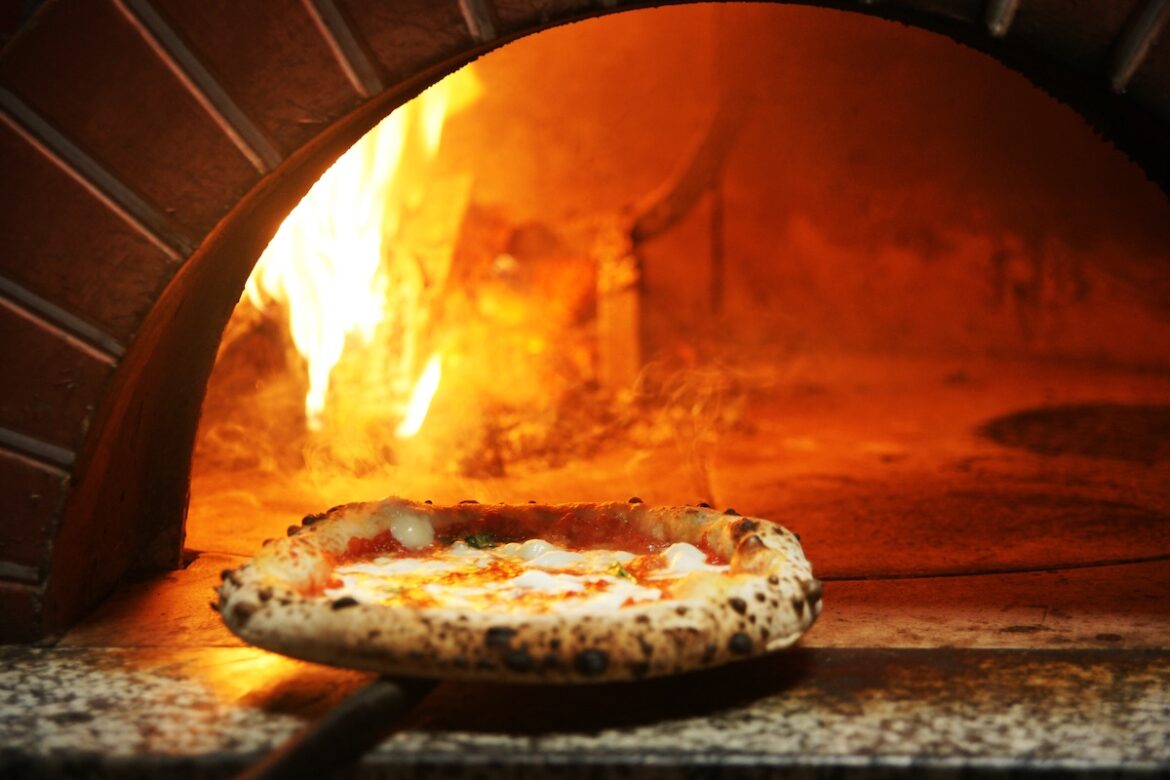 Why Italian Cuisine Is Set to Be Named a Global Cultural Treasure by UNESCO This photo shows a beautiful Neapolitan pizza perched on the edge of a flaming wood-fired oven.