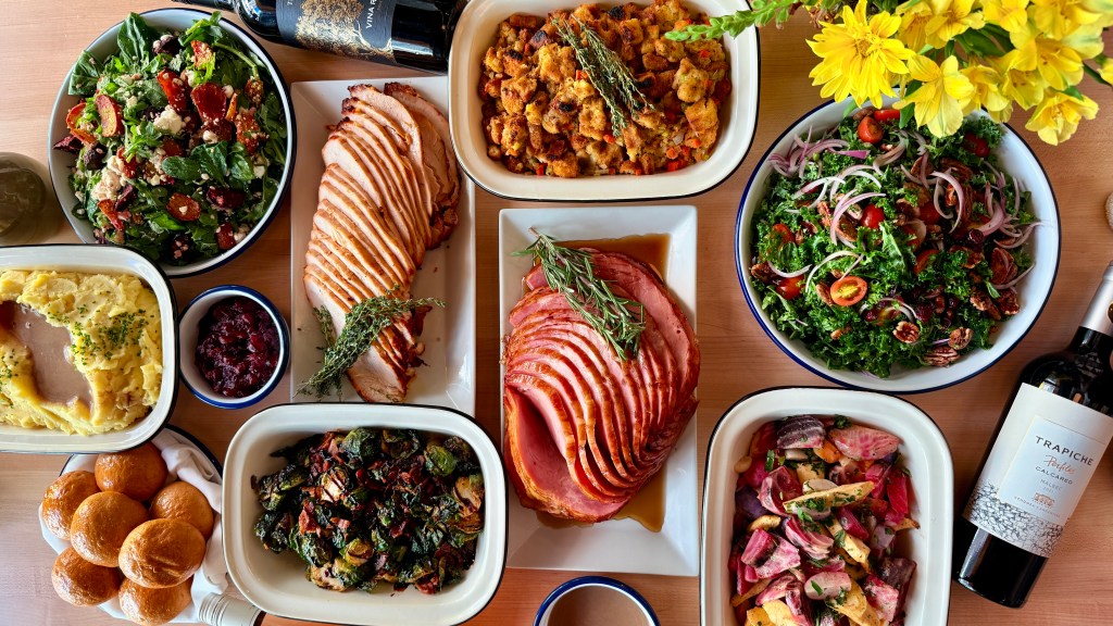 An overhead shot of sliced turkey, spiraled ham, stuffing, kale salad and more holiday dishes from Olive & Finch
