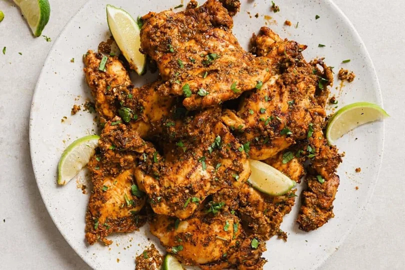Pollo asado on a white plate with lime wedges.