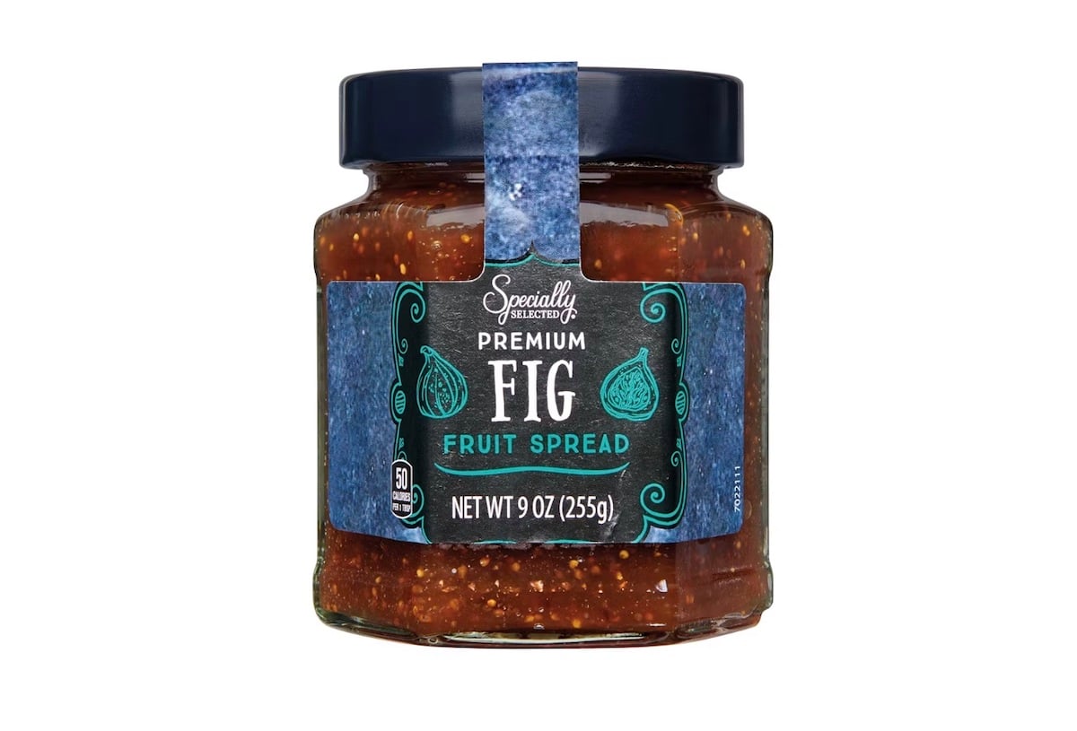 A jar of Specially Selected Premium Fig Fruit Spread with a dark blue lid and a blue label displaying fig illustrations. The jar contains 9 oz (255g) of the fruit spread.