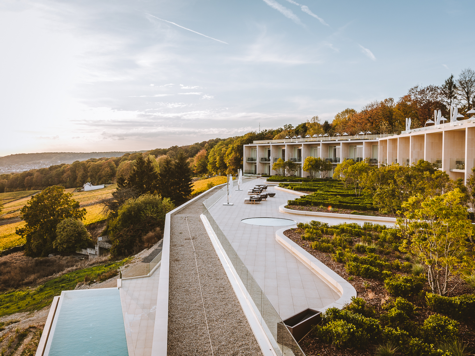A modern white hotel building sits low over a hillside with an infinity pool. 