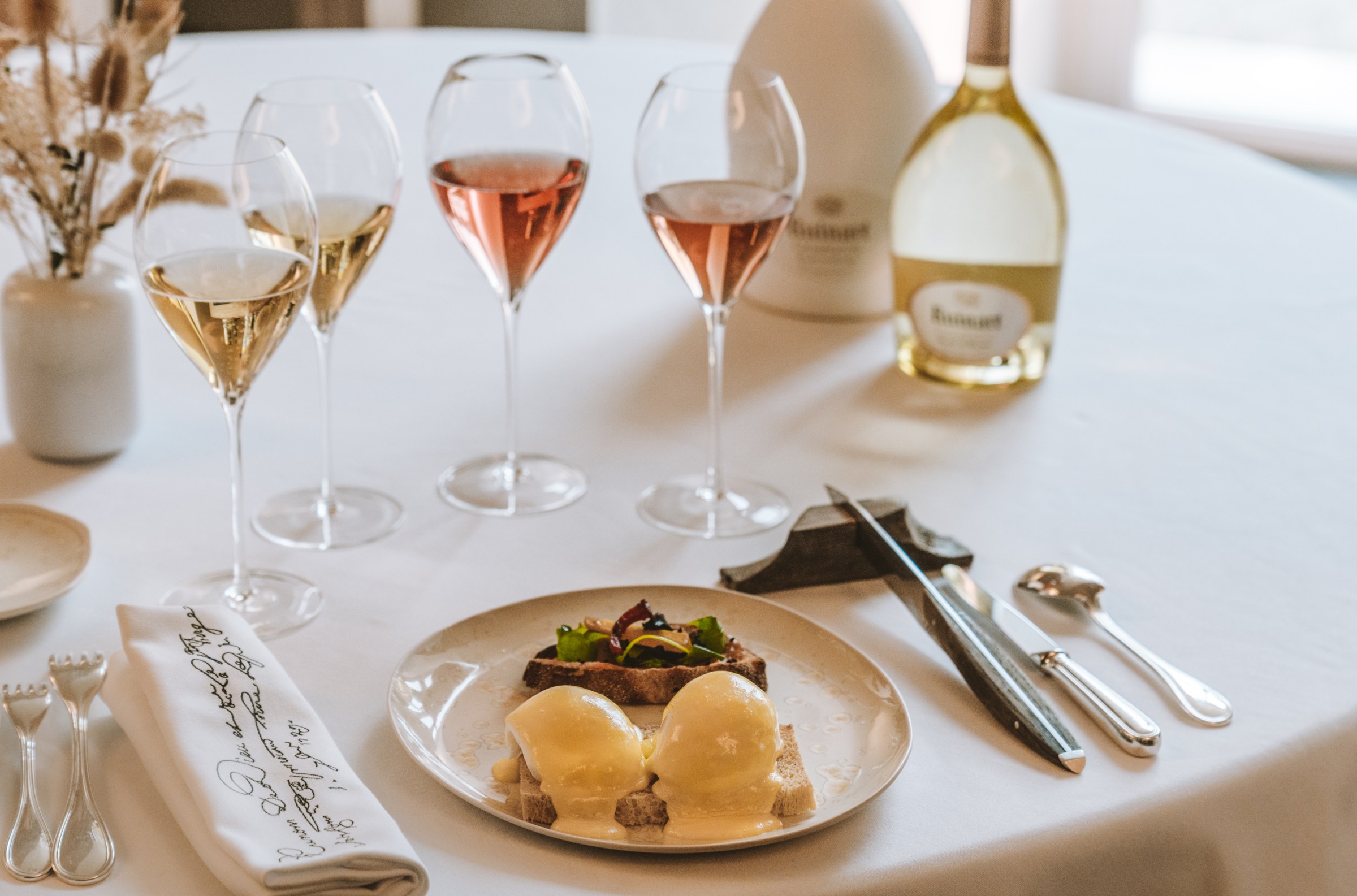 Poached eggs and several glasses of champagne sit on a fancy white tablecloth. 