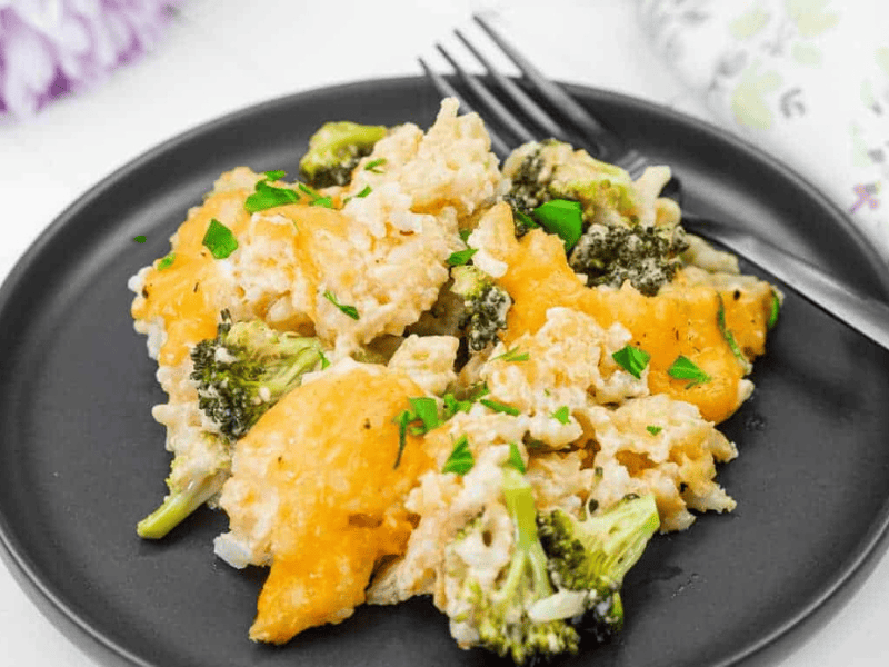 A serving of Broccoli Rice Casserole with Fresh Broccoli on a black plate.