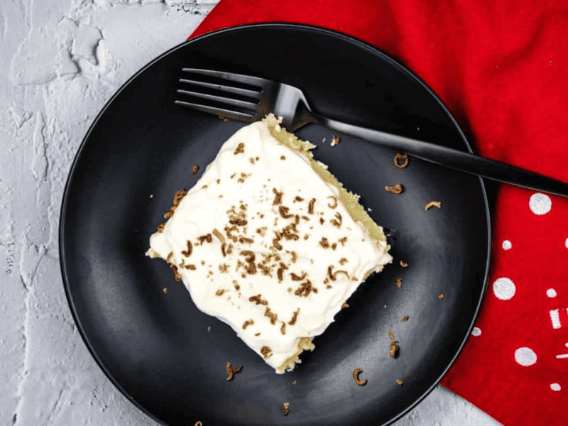A piece of eggnog tres leches cake on a black plate with a fork.