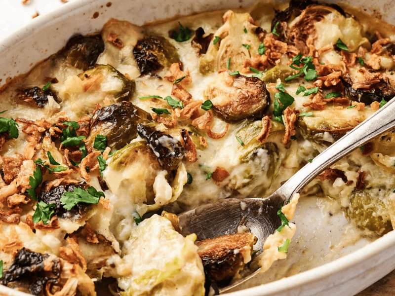Casserole dish with Brussels sprouts, crispy onions, cheese, and herbs, mixed with a spoon.