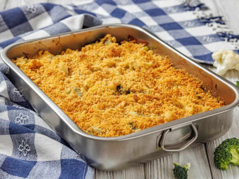 A rectangular baking dish filled with baked casserole topped with a golden breadcrumb crust sits on a blue and white checkered cloth.