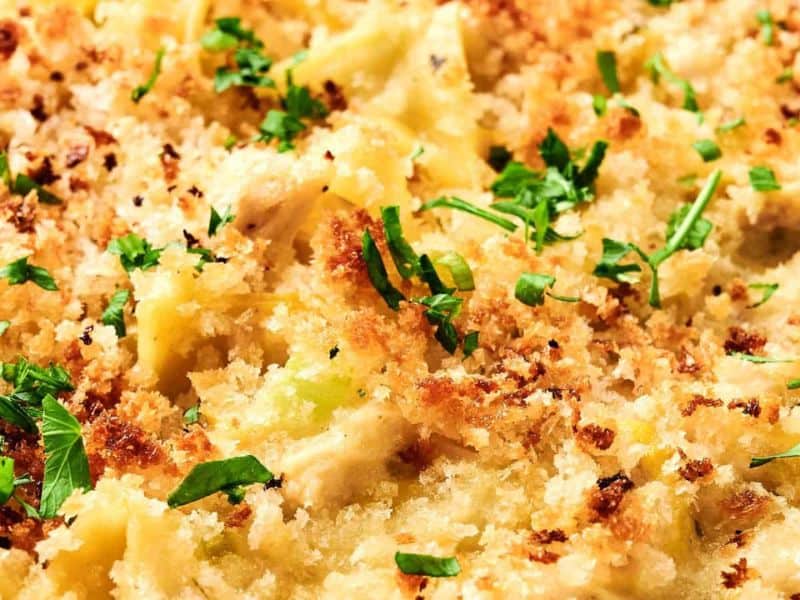 Close-up of a chicken noodle casserole with a golden breadcrumb topping, garnished with chopped herbs.