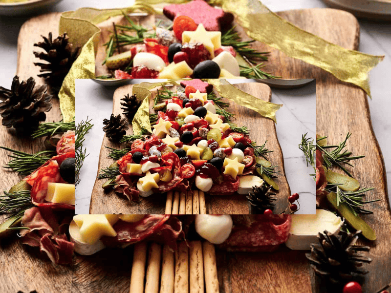Charcuterie board arranged in the shape of a Christmas tree with cheese, meats, berries, tomatoes, and herbs, placed on a wooden board with pinecones and ribbon nearby.