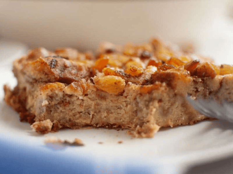 A close-up of a slice of Cinnamon Roll Casserole topped with golden raisins on a white plate.