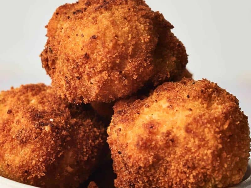 A bowl of golden-brown, crispy fried arancini served in a white dish on a plain background.