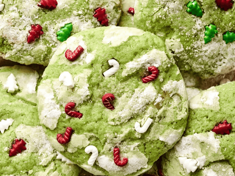 Green cookies topped with powdered sugar and red, green, and white candy shapes resembling trees and candy canes.