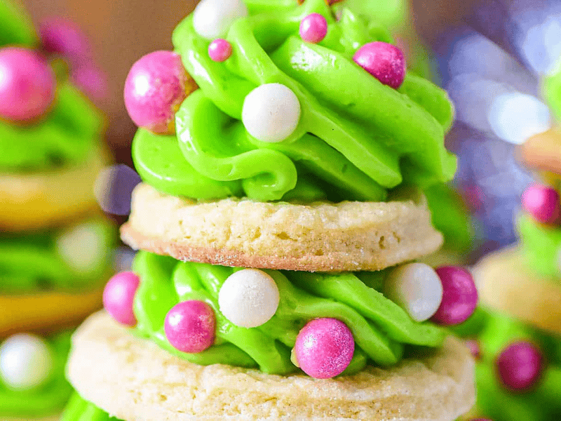 A festive cookie stack resembling a Christmas tree, decorated with green frosting and pink and white edible pearls.
