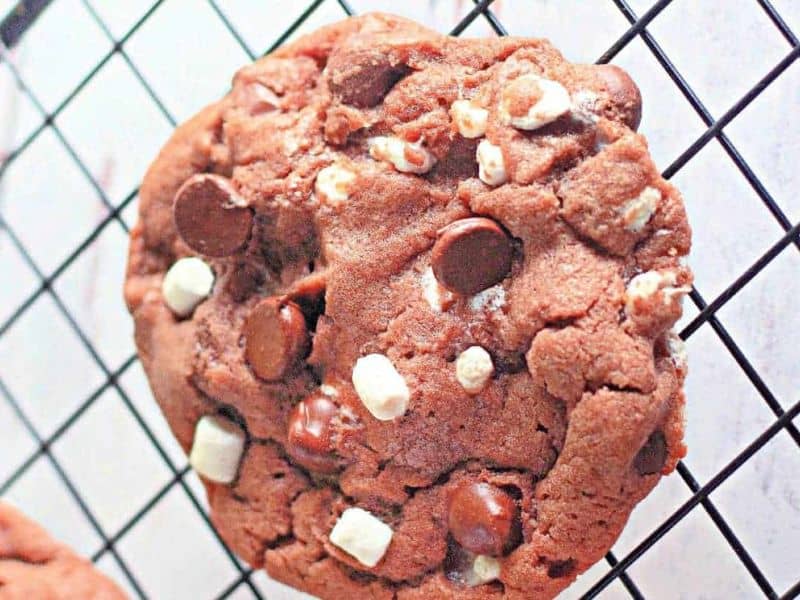 A close-up of a cocoa chip cookie with white and dark chocolate chunks resting on a black cooling rack.