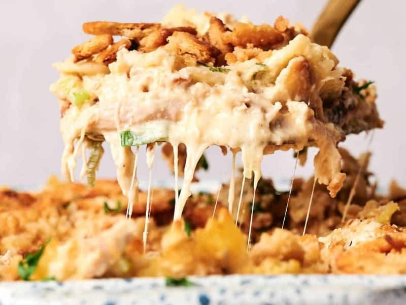 A serving spoon lifts a portion of creamy, baked casserole with a crunchy topping, revealing melted cheese.